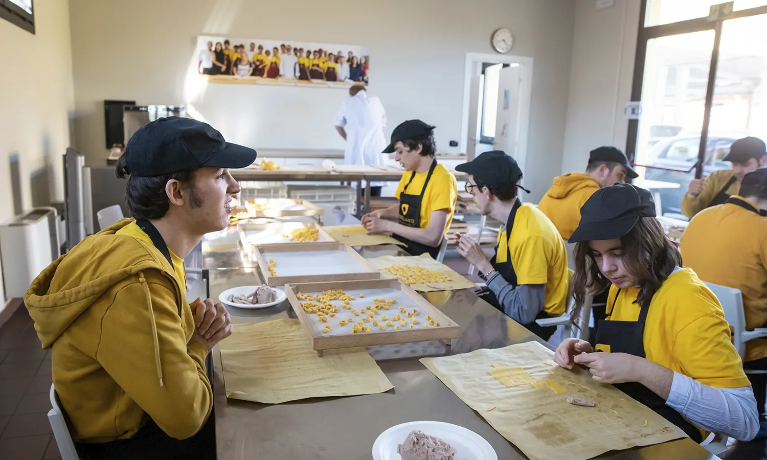 I ragazzi e le ragazze del Tortellante siedono ai tavoli di lavoro per preparare i tortellini.